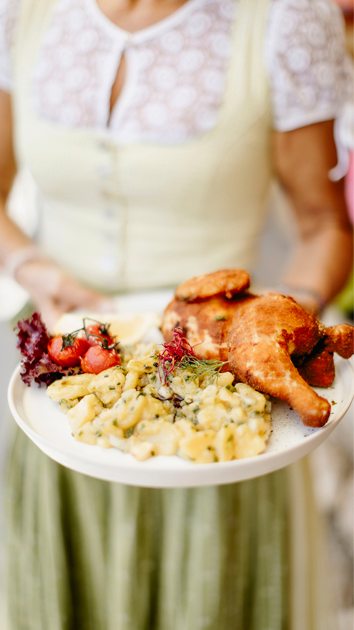 Kellnerin im Dirndl mit Grillhuhn und Beilage am Teller